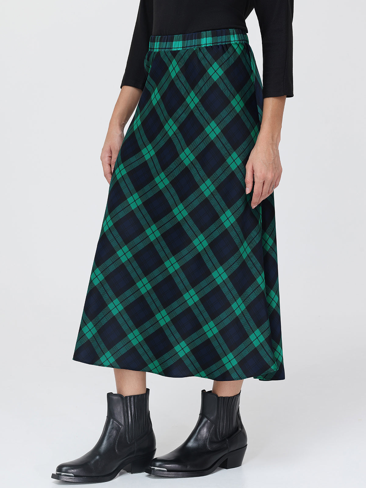 Person wearing a green and navy plaid skirt with black boots on a white background