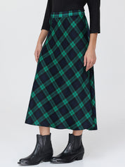 Person wearing a green and navy plaid skirt with black boots on a white background
