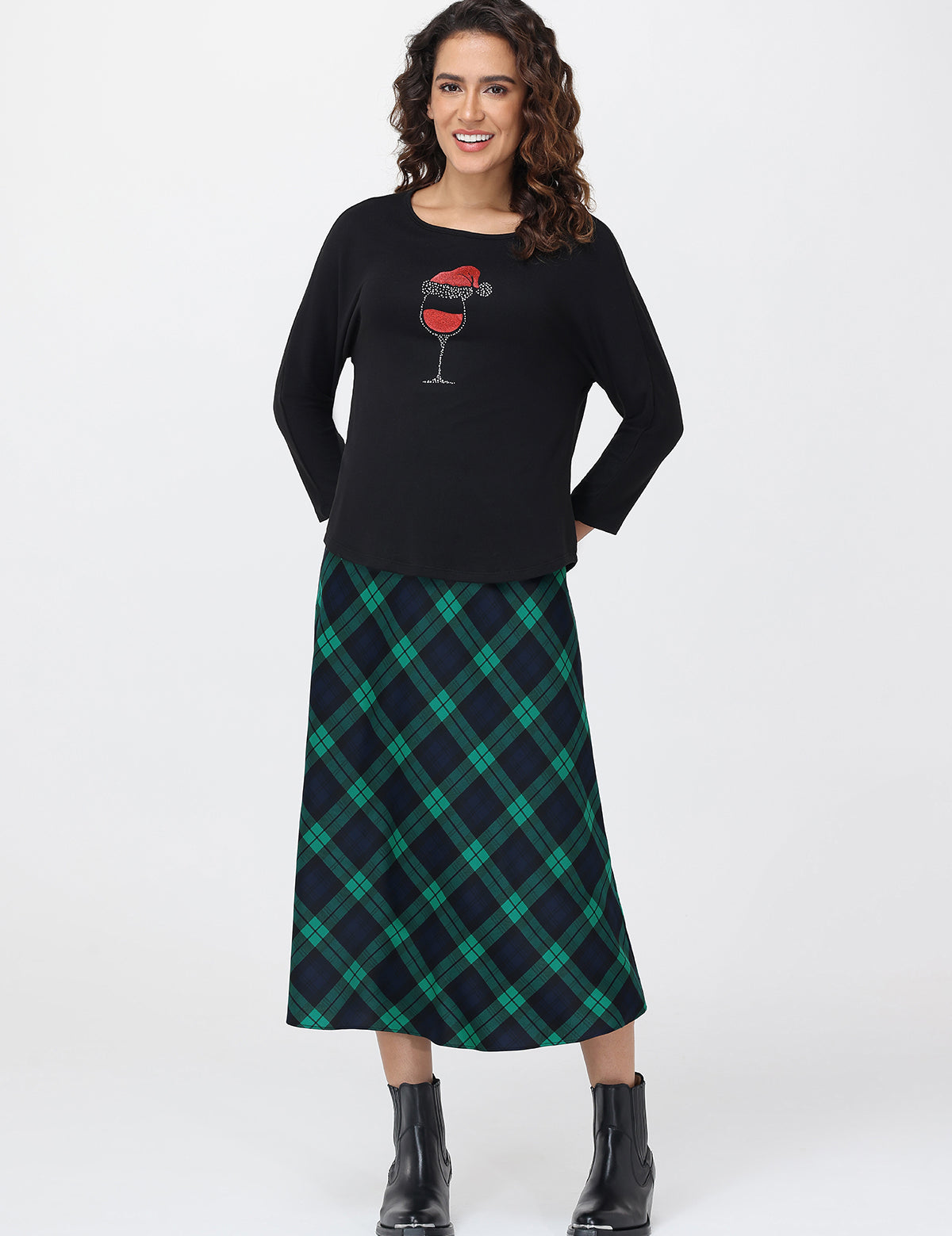 Woman wearing a black sweater with a graphic design and a green plaid skirt on a white background