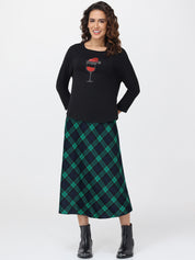 Woman wearing a black sweater with a graphic design and a green plaid skirt on a white background