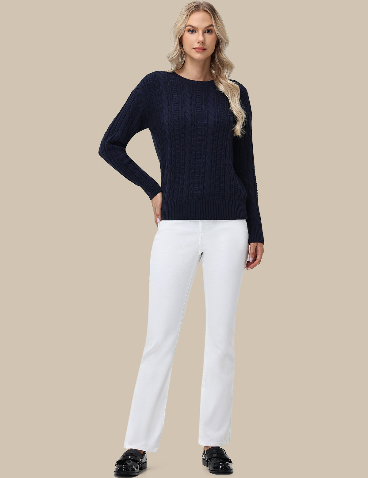 Woman wearing a navy sweater and white pants on a beige background