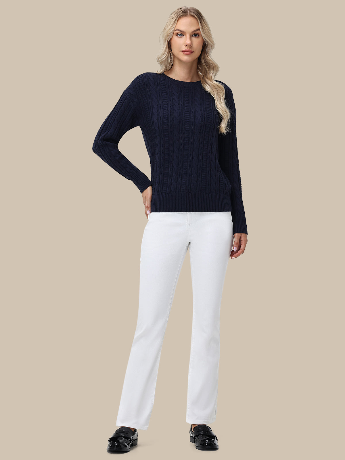 Woman wearing a navy sweater and white pants on a beige background