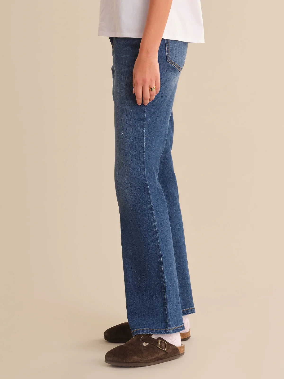 Person wearing blue jeans and brown shoes on a beige background