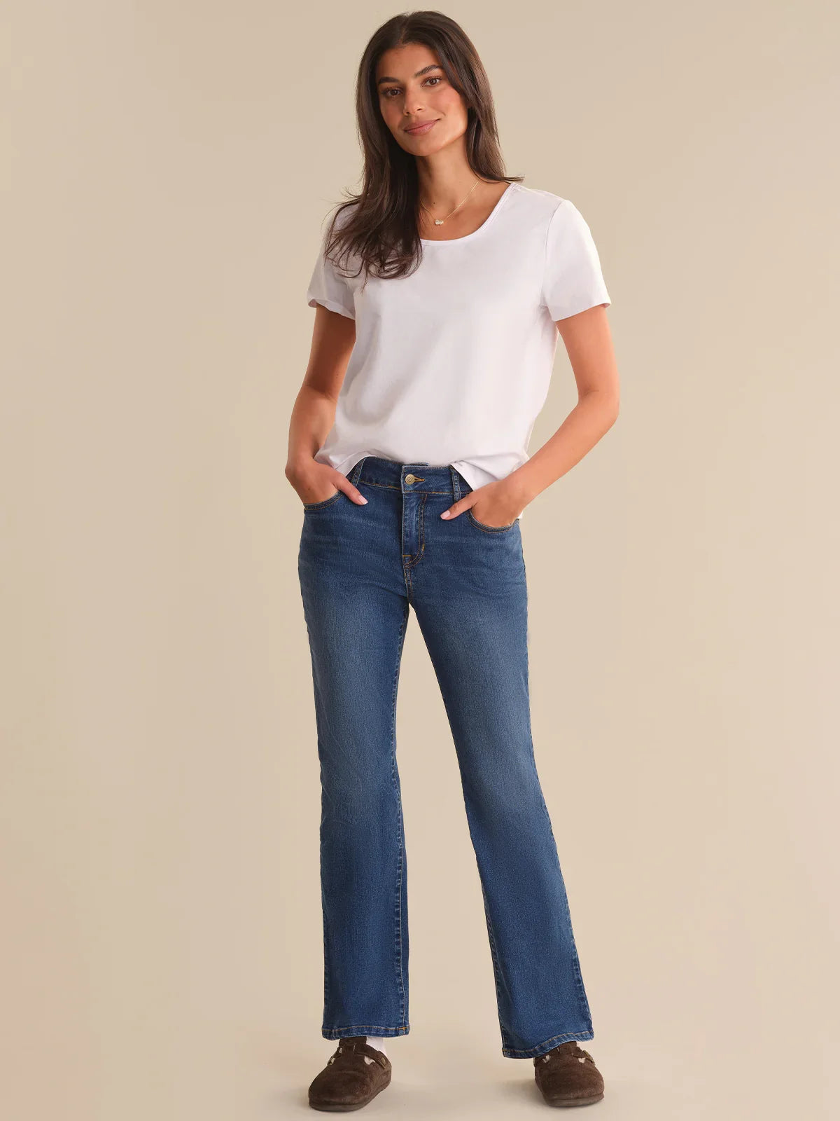 Woman wearing a white t-shirt and blue jeans on a beige background