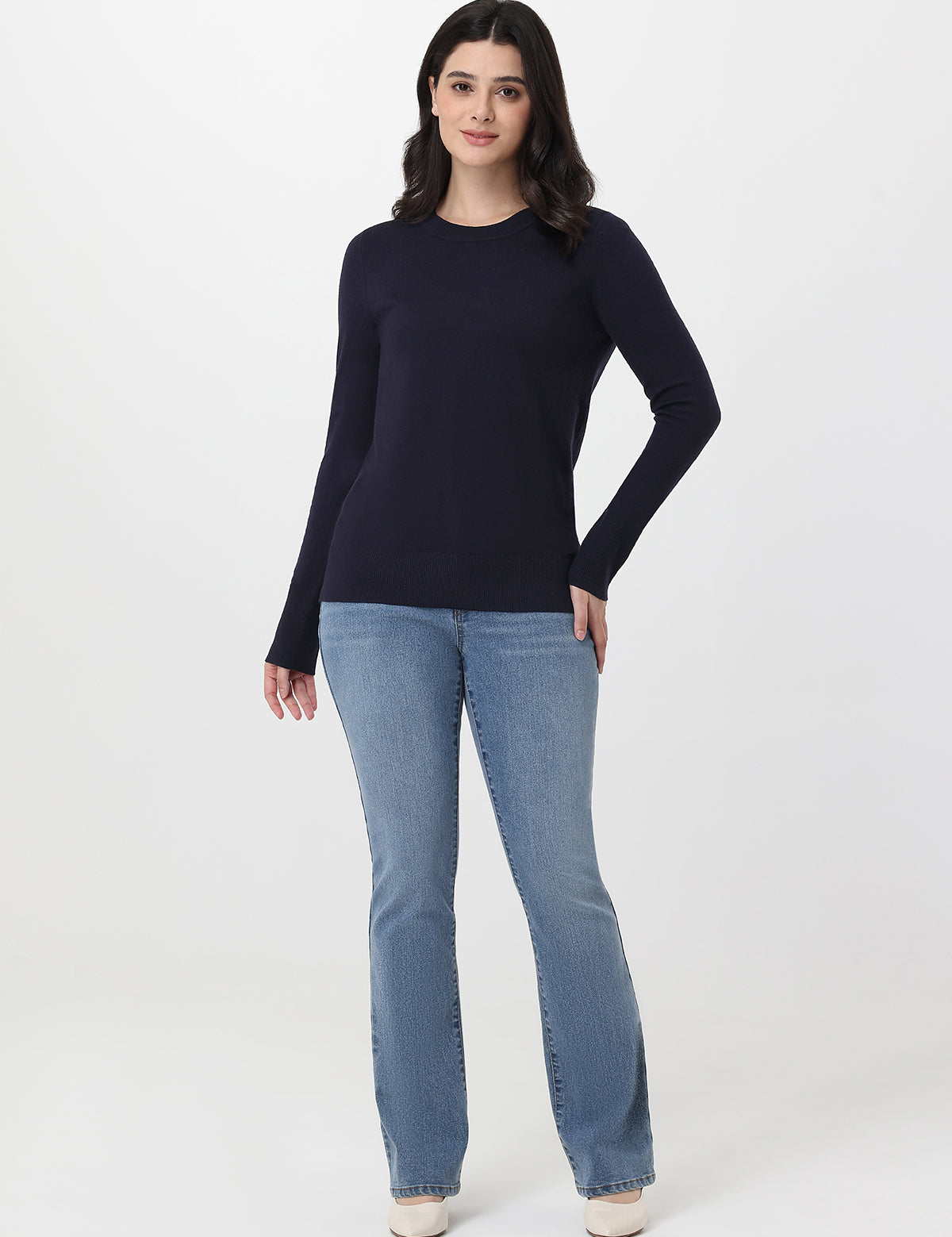 Woman wearing a navy sweater and light blue jeans on a white background