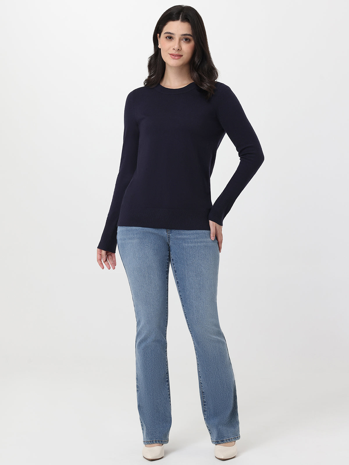 Woman wearing a navy sweater and light blue jeans on a white background