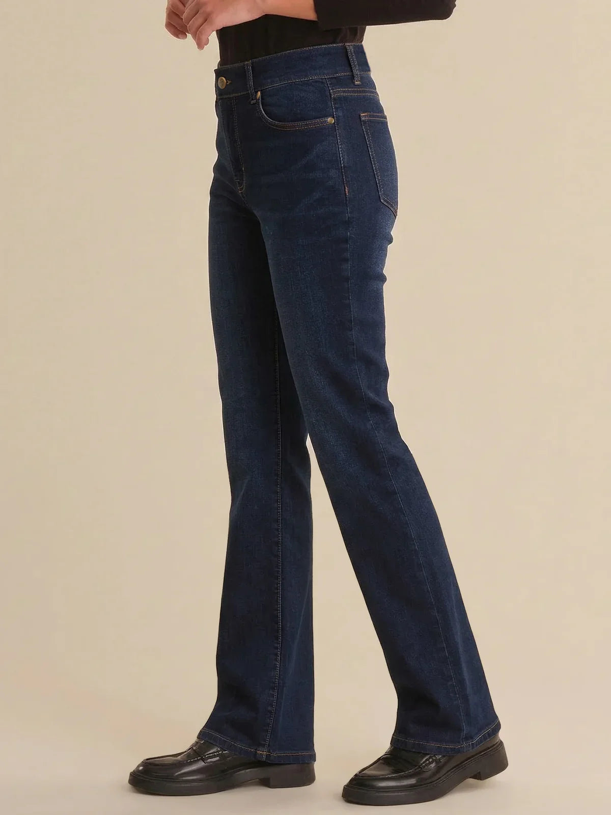 Person wearing dark blue jeans on a beige background