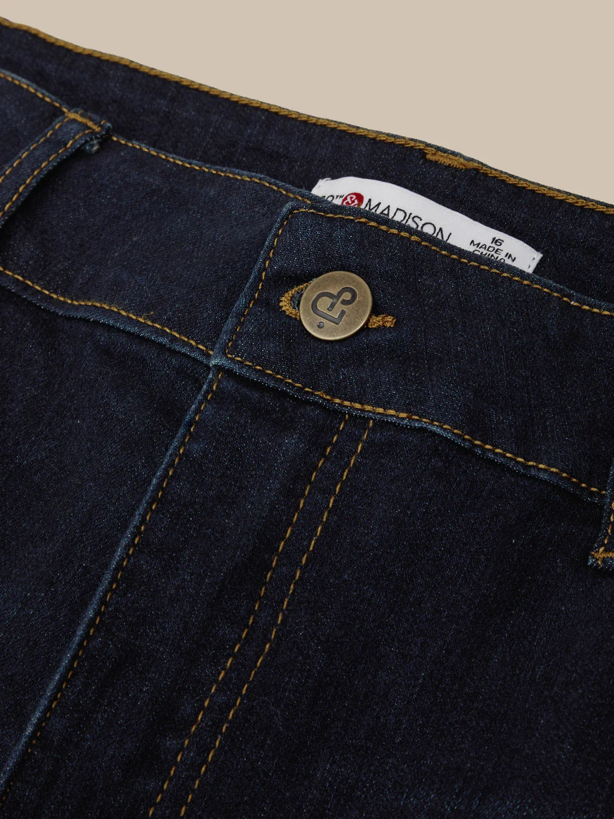 Close-up of dark blue denim fabric with a button and label on a beige background