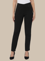 A model wearing slim-fit black trousers with a white top and black pointed-toe heels, shown against a solid beige background.