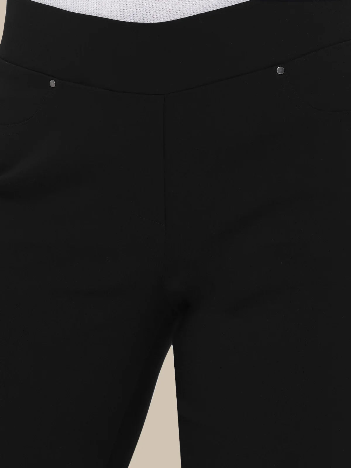 Close-up of black pants showing the waistband, front seam, and part of the leg, photographed against a light neutral background.
