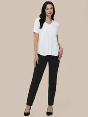 A woman modeling a white short-sleeve V-neck top and black pants against a solid beige background.