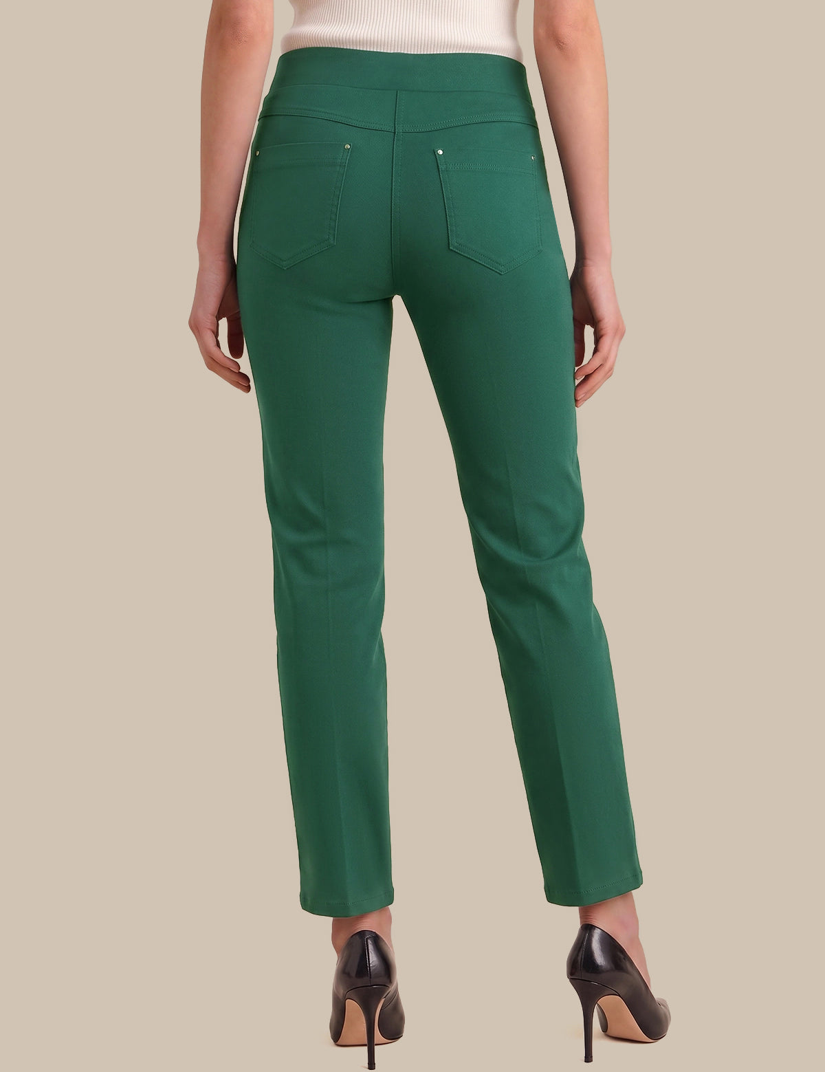 A model shown from the back wearing a pair of slim-fit green trousers with a high waistband, back pockets, and a straight leg, paired with black high heels against a solid beige background.