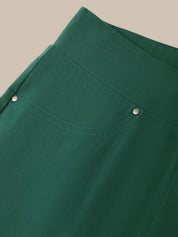Close-up of a dark green garment, likely a skirt or dress, showing a curved seam, a decorative pocket with silver-tone snap details, and a clean beige background.