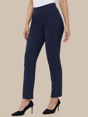 A model wearing navy blue cropped trousers with a white top and black high heels, shown from the waist down against a solid beige background.