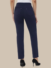A person shown from the back wearing navy blue high-waisted straight-leg pants with silver button details on the back pockets, paired with black high heels against a solid beige background.