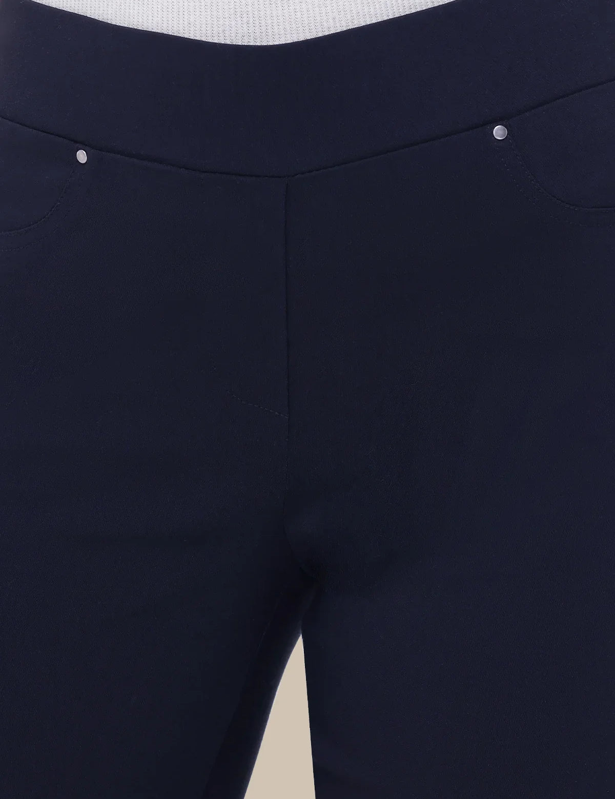 Close-up of dark navy blue pants showing the waistband, front seam, and a small silver rivet detail.