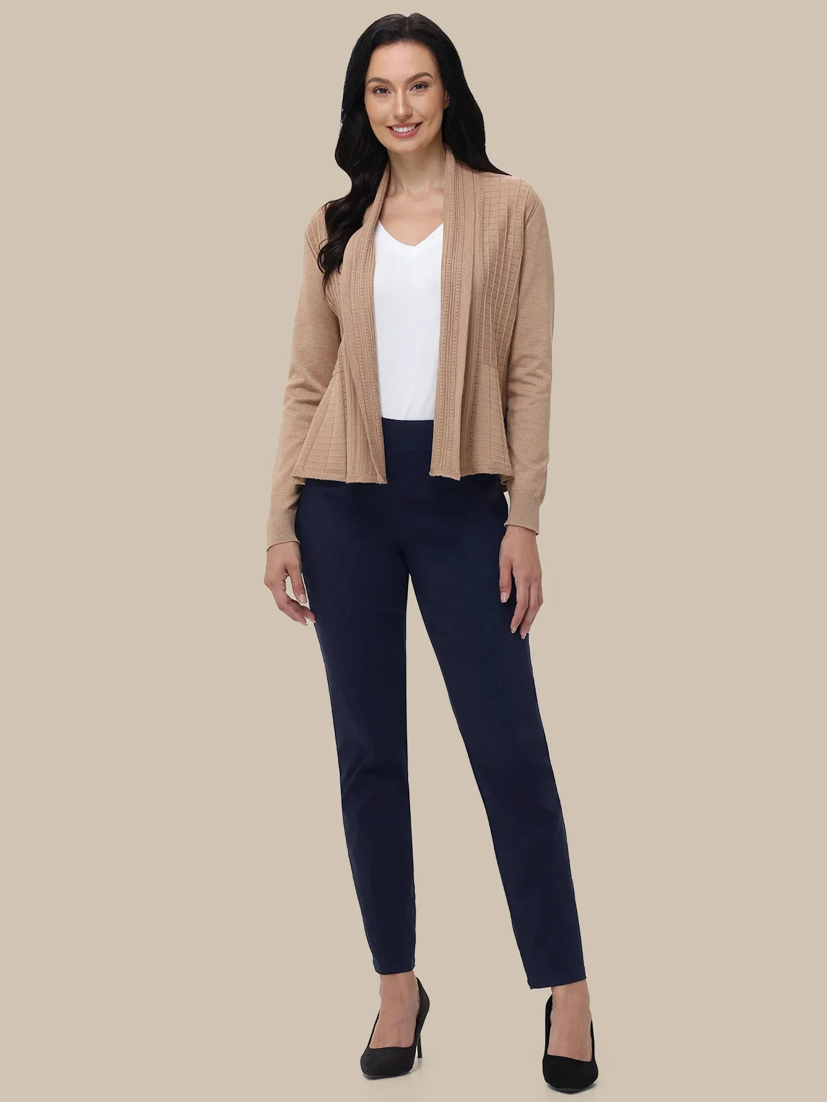 A woman modeling a beige open-front cardigan over a white top and navy blue pants, paired with black heels, against a solid beige background.