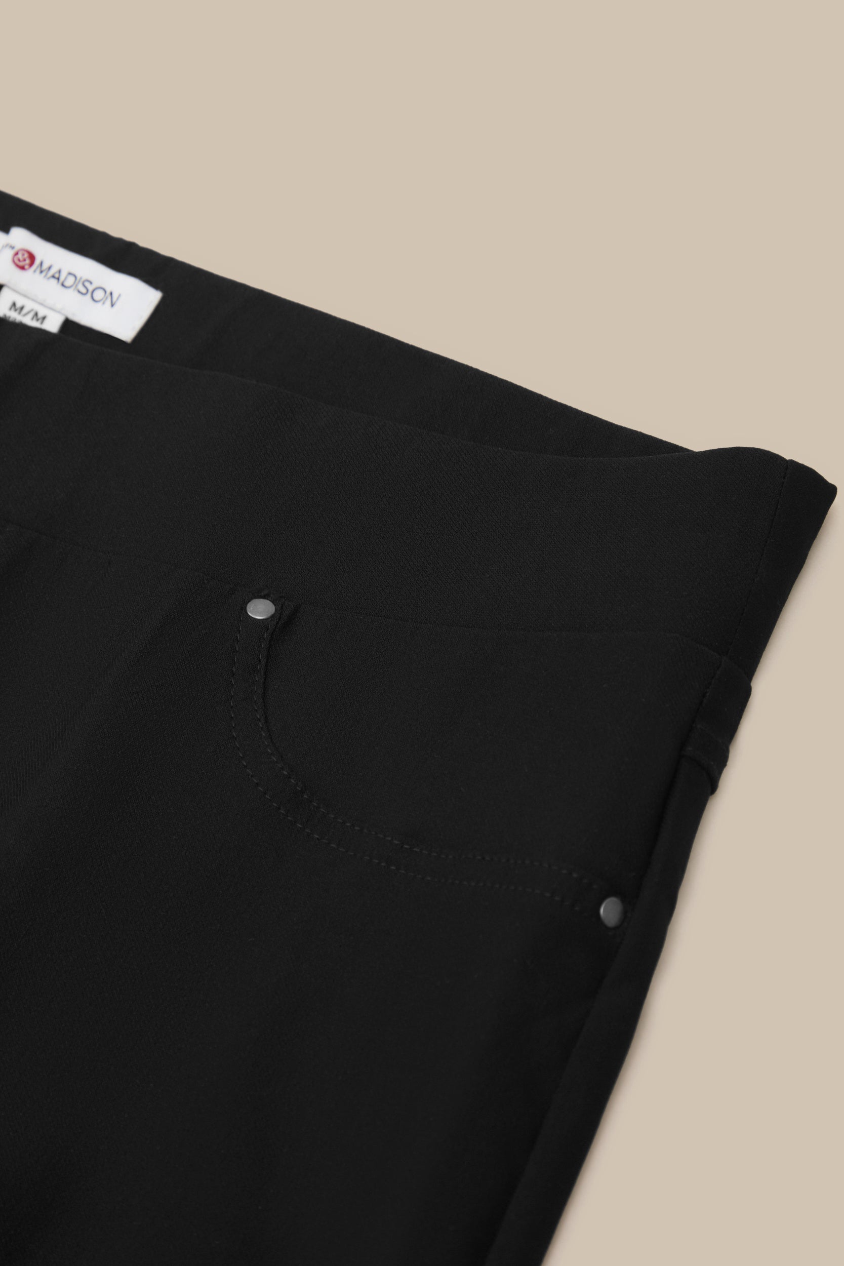 Close-up of black pants with a Mansur Gavriel label on a beige background