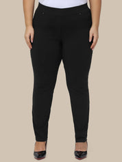 A model wearing black slim-fit pants with a wide elastic waistband, paired with a white top and black pointed-toe heels, shown against a solid beige background.