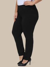 A model wearing black slim-fit pants with a white top and black patent leather heels, shown from the waist down against a solid beige background.