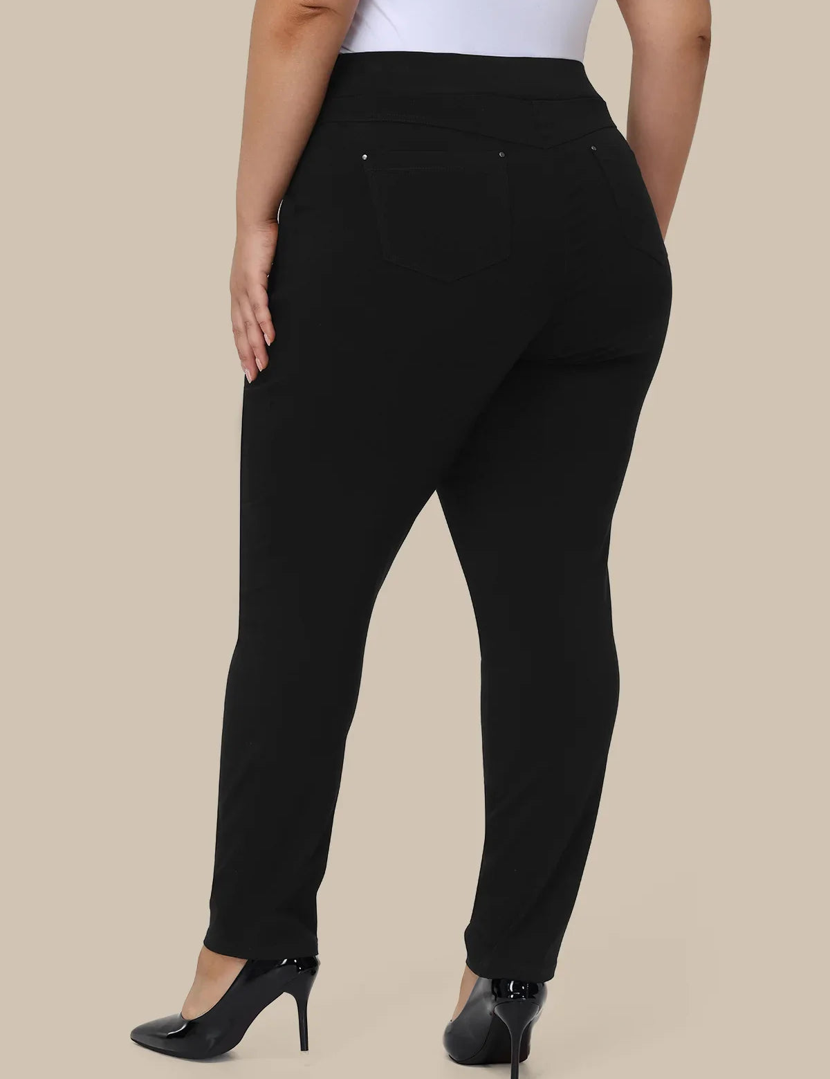 A model shown from the back wearing black high-waisted slim-fit pants with a white top and black heels, set against a solid beige background.