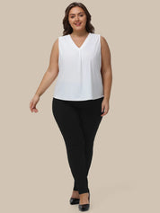 A woman modeling a sleeveless white V-neck top paired with black pants and black heels, standing against a solid beige background.