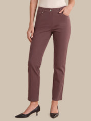 A model wearing slim-fit, ankle-length trousers in a muted dusty rose or mauve color, paired with black pointed-toe heels and a light-colored top, set against a solid beige background.