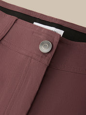 Close-up detail of mauve-brown trousers showing a button closure, waistband, and fabric texture against a neutral beige background.