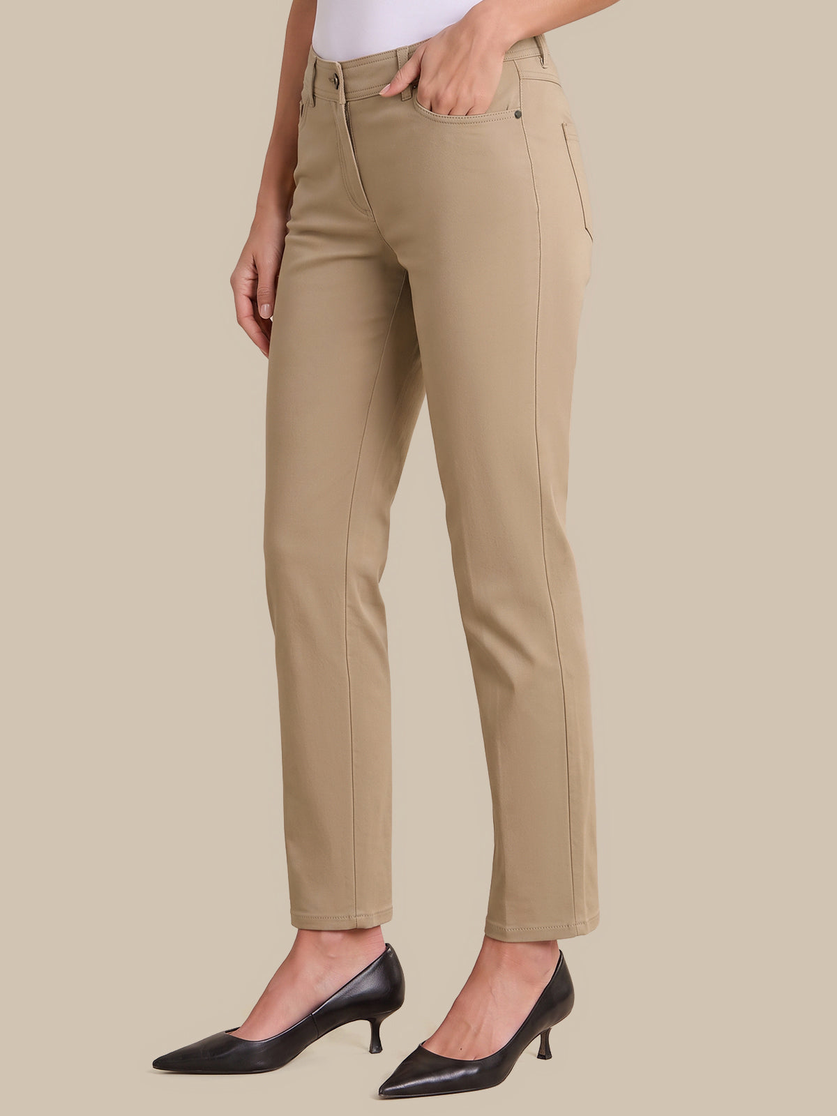 A model wearing beige straight-leg cropped pants with a white top and black pointed-toe heels, shown from the waist down against a solid beige background.
