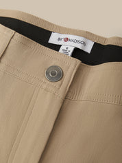 Close-up of beige trousers showing the waistband, a silver metal button, and a white brand label reading 89 Madison.