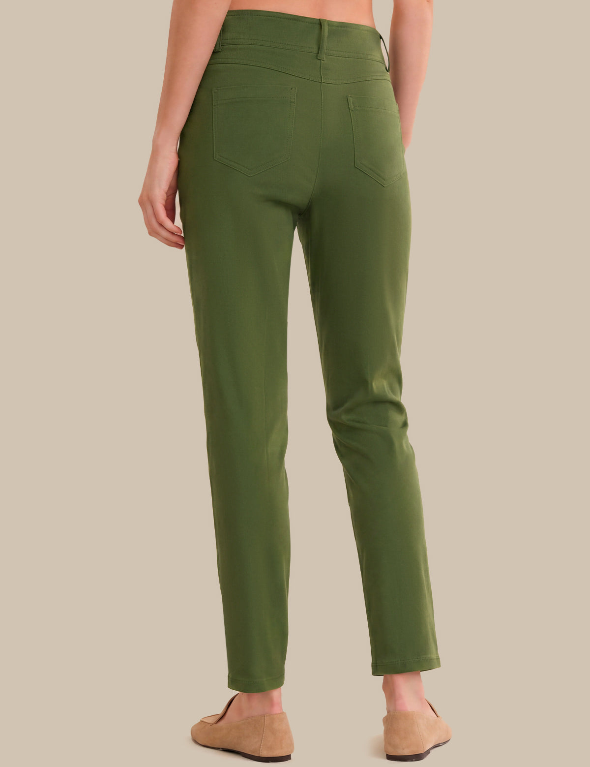 A person shown from the back wearing olive green slim-fit pants and tan slip-on shoes against a plain beige studio background.