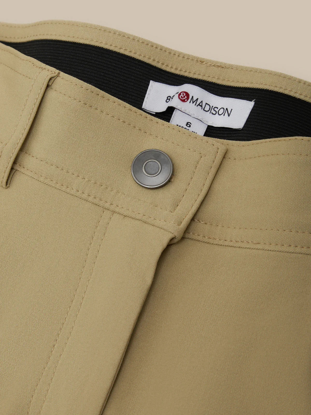 Close-up of beige pants with a button and brand label, featuring 'Madison' branding.