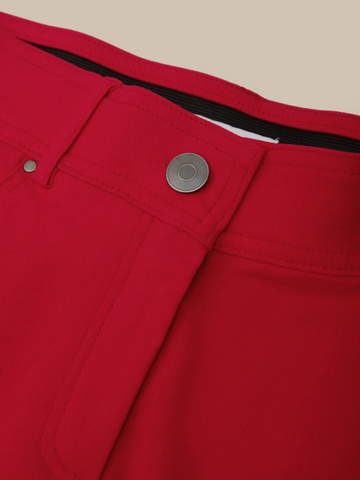 Close-up of a red pants pocket with a button and zipper on a beige background