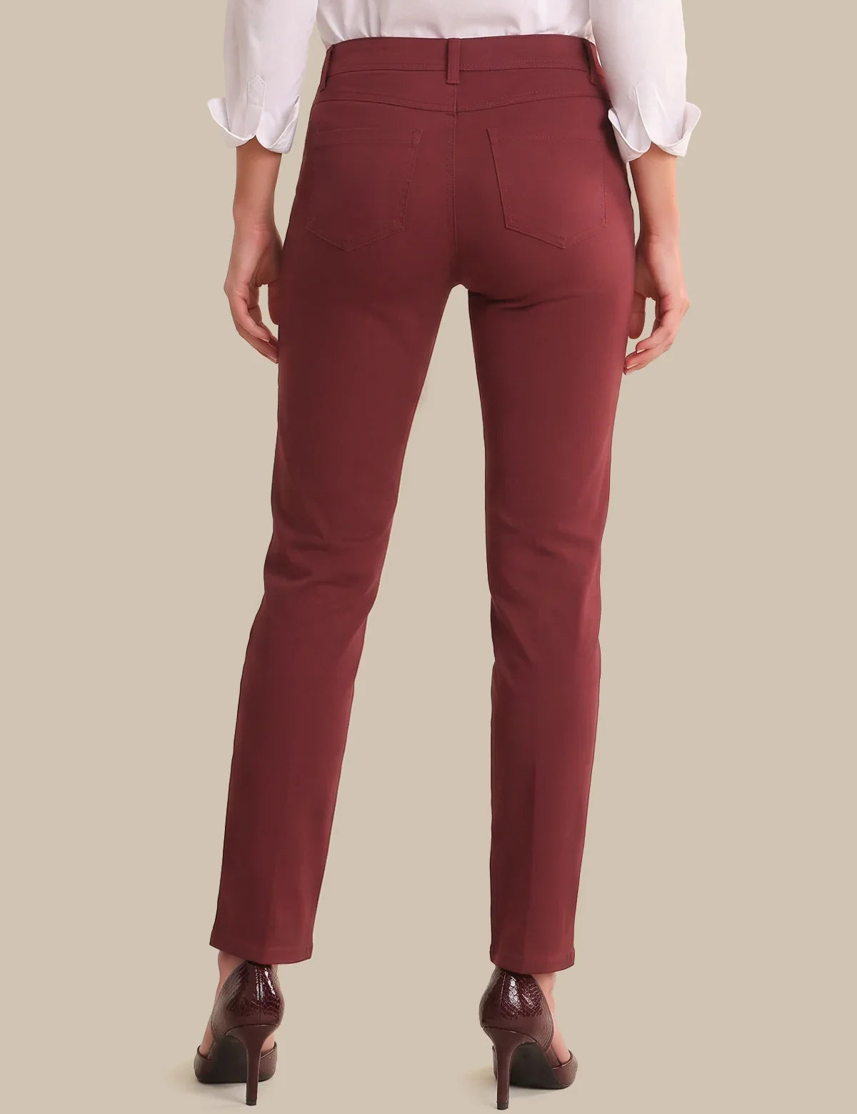 A person shown from the back wearing slim-fit burgundy trousers, a white blouse with rolled sleeves, and dark brown high heels against a plain beige studio background.