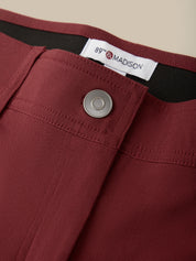 Close-up of burgundy trousers showing the waistband, a silver metal button, and a white interior label reading 89th & MADISON.