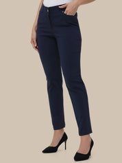 A model wearing navy blue slim-fit ankle-length trousers, styled with a white top and black high heels against a solid beige background.