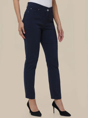A model wearing a pair of dark navy blue slim-fit ankle-length jeans with a white top and black high heels, shown from the waist down against a solid beige background.