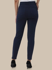 A person shown from the back wearing slim-fit navy blue pants, a white top, and black high heels against a plain beige studio background.