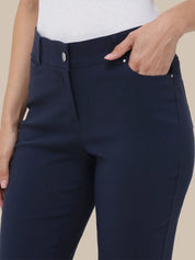 Close-up of a person wearing dark navy blue slim-fit pants, with a hand resting in the front pocket. The model is also wearing a white ribbed top, set against a solid beige background.