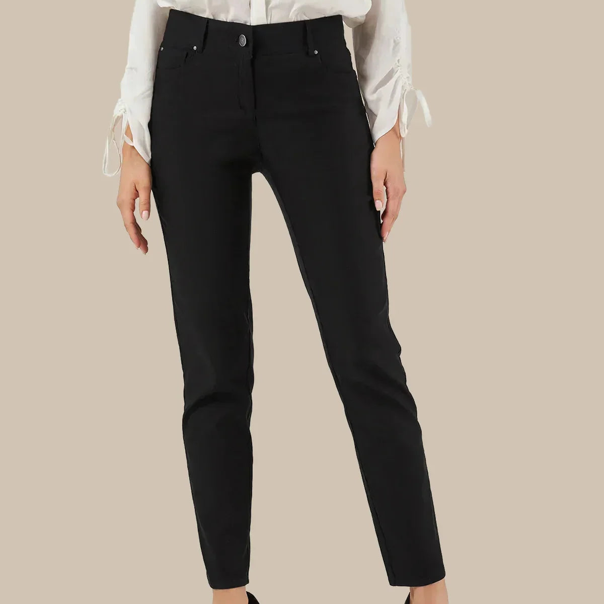 A model wearing black straight leg pants with a white long-sleeve blouse and black pointed-toe heels, shown against a solid beige background.