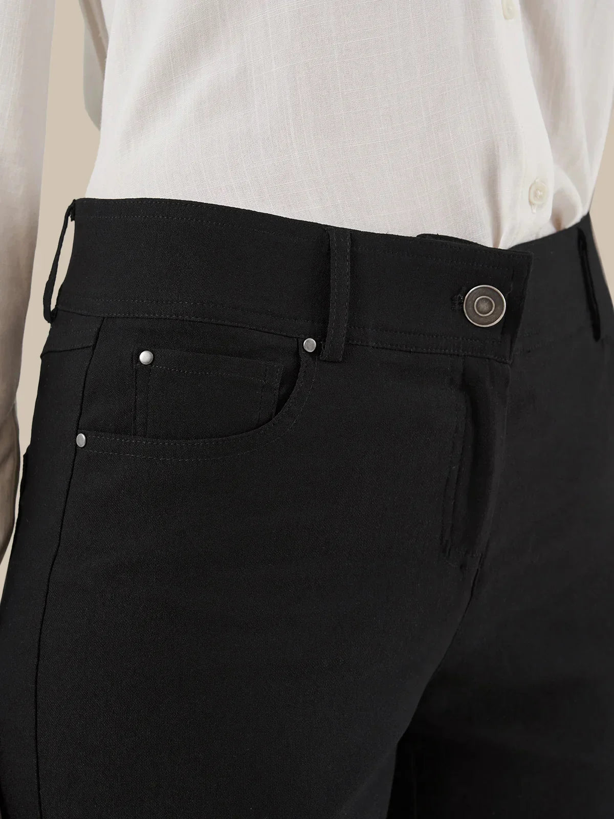 Close-up of a person wearing black trousers with a white shirt tucked in, showing the waistband, button, belt loops, and front pocket.
