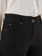 Close-up of a person wearing black trousers with a white shirt tucked in, showing the waistband, button, belt loops, and front pocket.