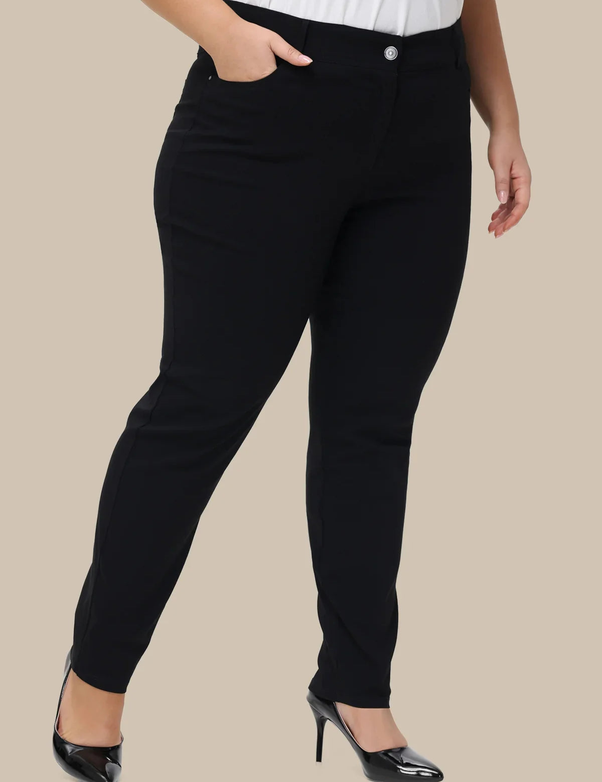 Black slim-fit pants shown on a model from the waist down, paired with a white top and black patent high heels, against a solid beige background.