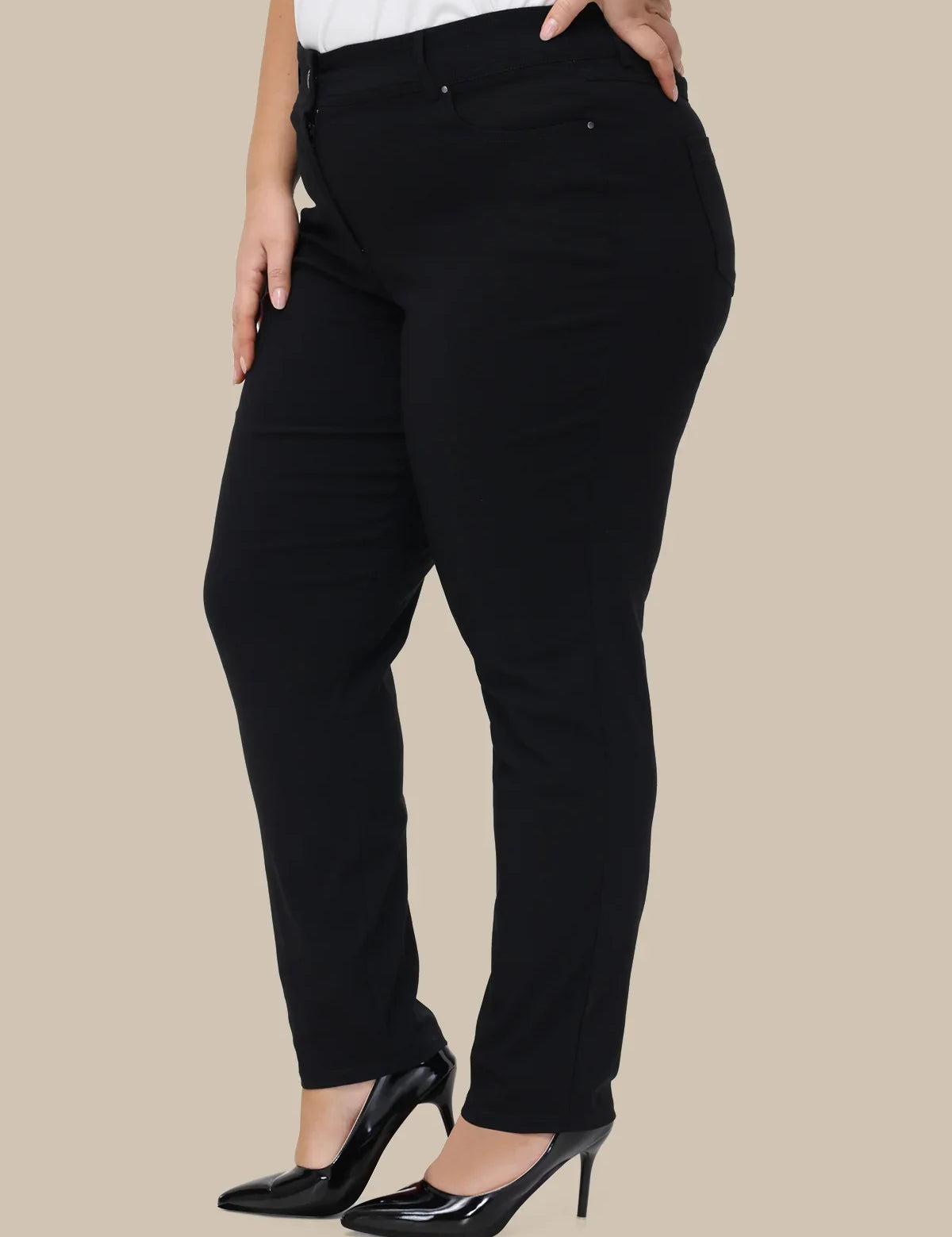 A model wearing black slim-fit pants with a white top and black patent leather pumps, shown from the waist down against a solid beige background.