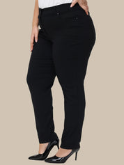 A model wearing black slim-fit pants with a white top and black patent leather pumps, shown from the waist down against a solid beige background.
