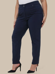 A model wearing navy blue slim-fit trousers with a white top and black high heels, shown from the waist down against a solid beige background.