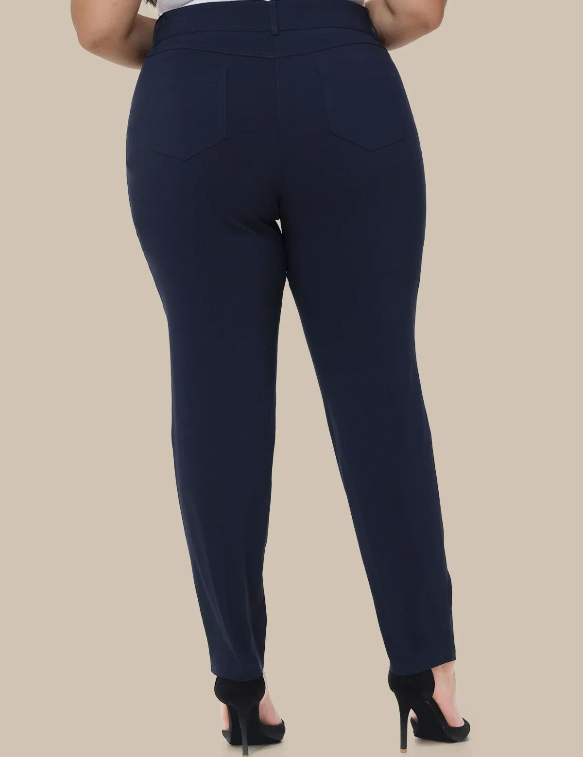 A person shown from the back wearing navy blue slim-fit trousers with a high waist and back pockets, paired with black high heels against a plain beige studio background.
