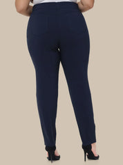 A person shown from the back wearing navy blue slim-fit trousers with a high waist and back pockets, paired with black high heels against a plain beige studio background.