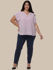 A woman modeling a light pink short-sleeve blouse with a split V-neck and dark navy pants, standing against a solid beige background.