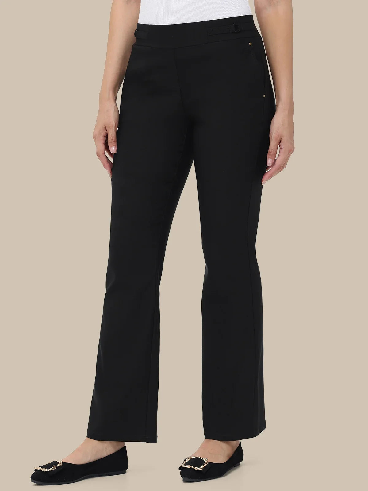 A model wearing black wide-leg cropped trousers with a white top and black flats, shown from the waist down against a solid beige background.